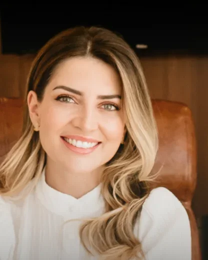 Dra. Pryscilla Marcon sorrindo, de blusa branca, numa poltrona de couro